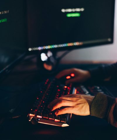 From above of crop anonymous cyber spy typing on computer keyboard with data on screen at night